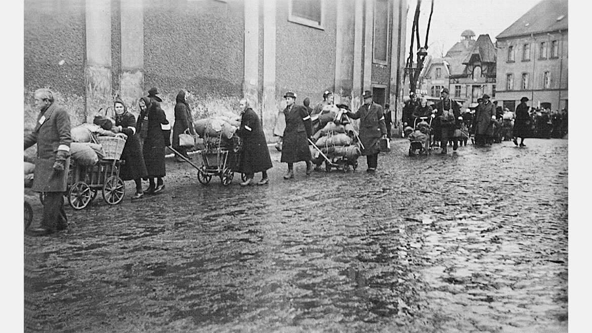 Vertreibung aus Schlesien, 1946: Zur Vertreibung der Deutschen durch polnische Behörden gehört nach einer Übereinkunft mit der britischen Besatzungszone auch die „Aktion Schwalbe“ von 1946. Davon betroffen waren Millionen Menschen in Schlesien, der bevölkerungsreichsten Provinz im ehemaligen Osten des Deutschen Reiches. Das Bild zeigt Niederschlesier im Februar 1946 vor der Minoritenkirche in Glatz auf dem Weg zum Bahnhof, von wo sie mit Viehwaggons nach Westen abtransportiert wurden. Deutlich sind die weißen Armbinden sichtbar, die sie als Deutsche kennzeichneten.