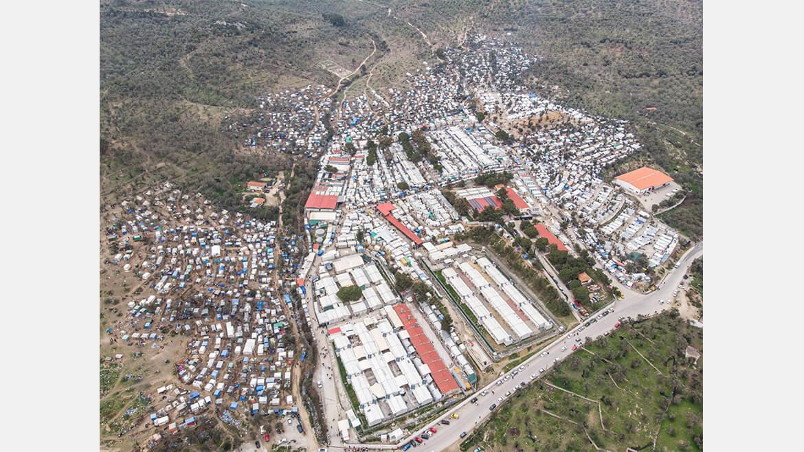 Lesbos, 2020: Viele Flüchtlinge legen weite Strecken zurück, bis sie in Sicherheit sind. Auf ihrem Weg stranden viele in Lagern und Transitzentren. Das Flüchtlingslager Moria auf der griechischen Insel Lesbos war eines von ihnen: Auf dieser Luftaufnahme ist die Überbelegung des Lagers sichtbar, improvisierte Behausungen gruppieren sich rund um das eigentliche Lager. 2020 brannte die Anlage vollständig ab. Die Menschen wurden in einem provisorischen Lager untergebracht – auch dieses neue Lager stößt bereits an die Grenzen seiner Kapazitäten...