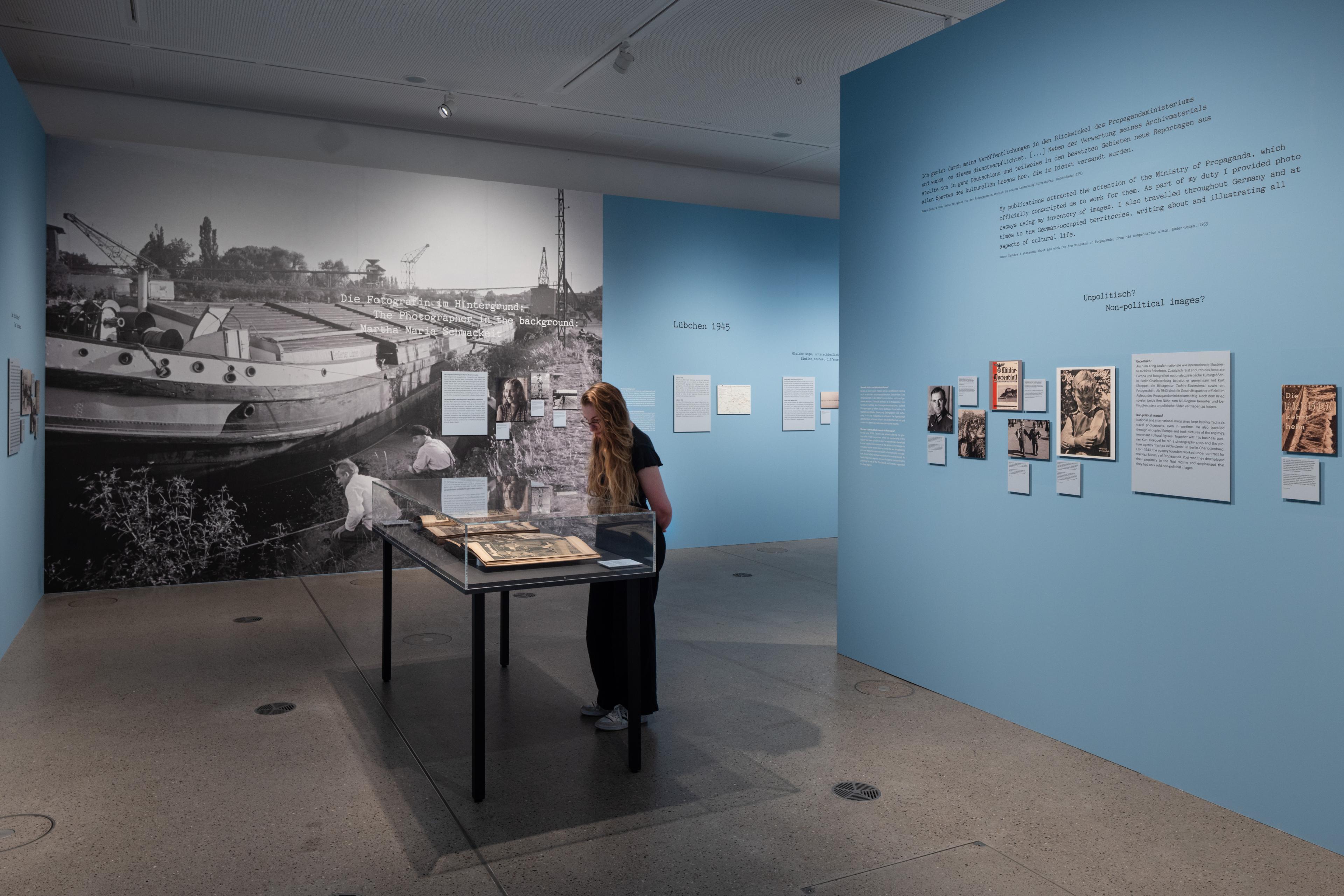Eine Frau, die die Ausstellung "Der Treck" anschaut, im Fokus ist eine Vitrine, auf die die Frau blickt.