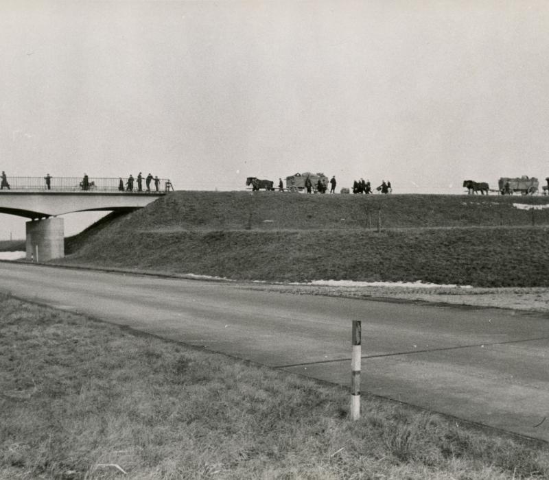 Schwarz-weiß Aufnahme einer Autobahn und darüber verlaufenden Brücke mit Menschen.