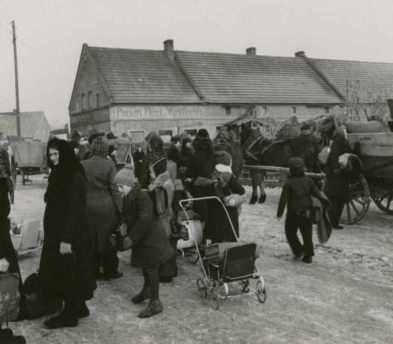 Schwarz-weiß Aufnahme einer Gruppe Menschen auf einem Dorfplatz.