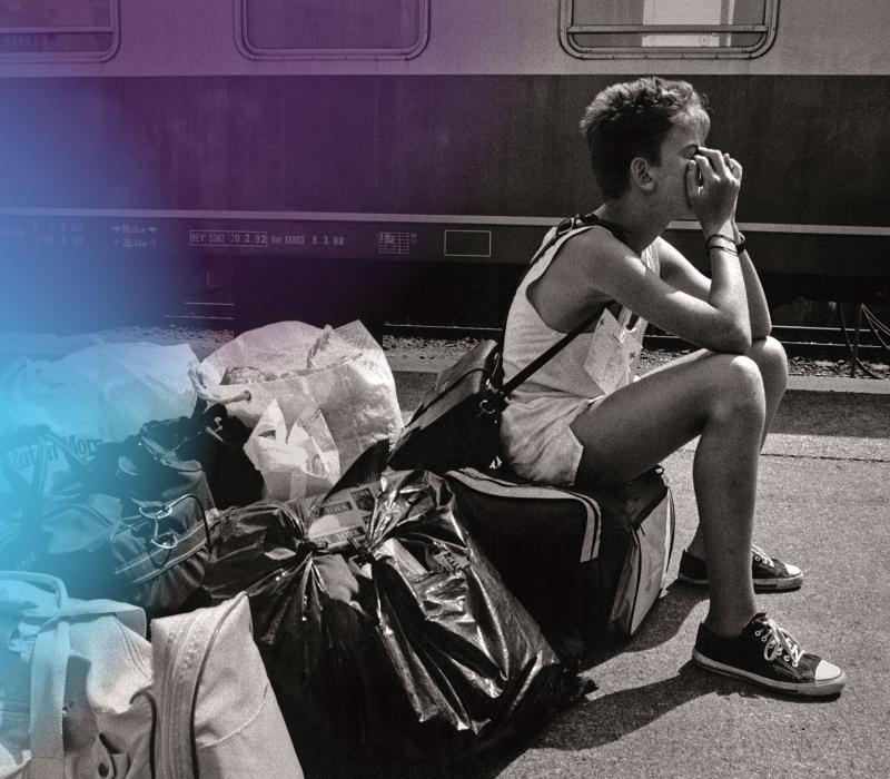 Schwarz-weiß Bild, ein Junge sitzt auf Gepäck an einem Bahngleis.