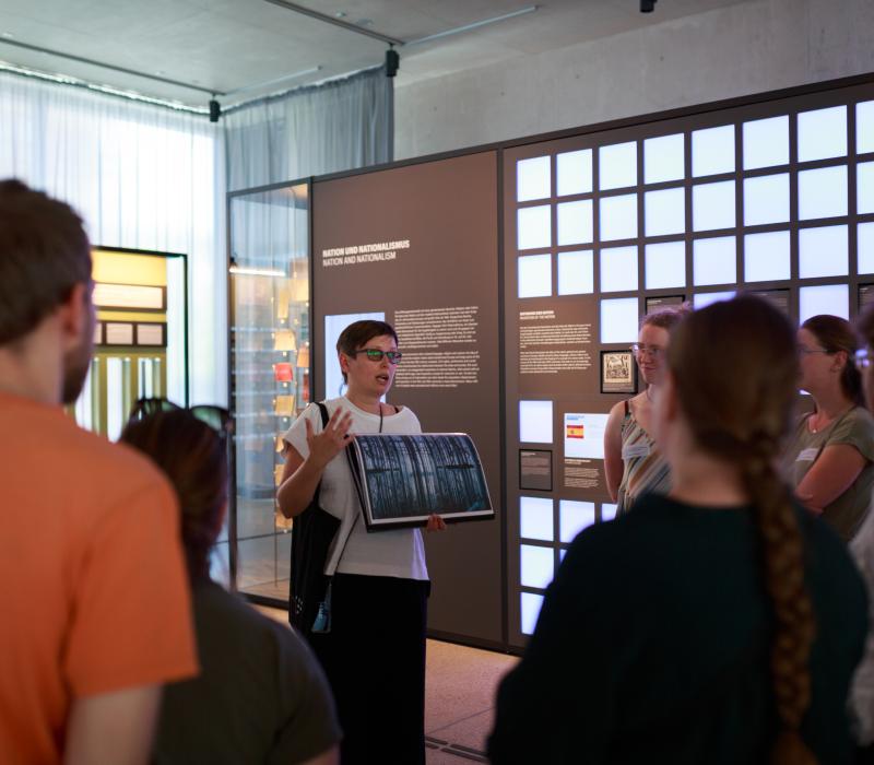 Eine Gruppe steht zusammen und schaut zu einer Person, die ihnen etwas erzählt.