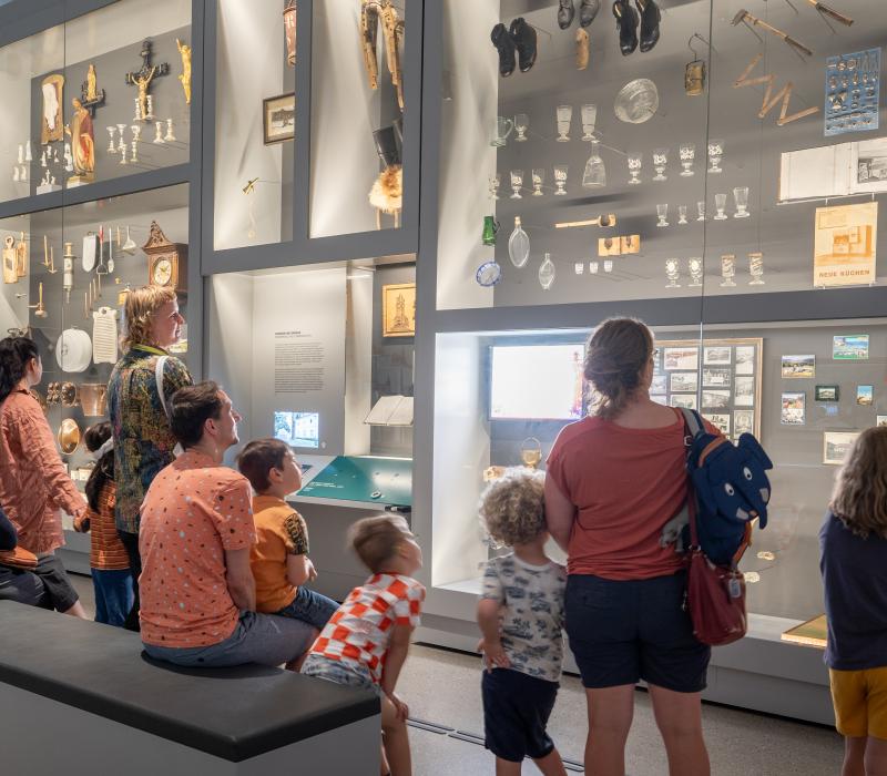 Eine Gruppe mit Erwachsenen und mehreren Kindern steht vor einer Wand mit beleuchteten Ausstellungsstücken.