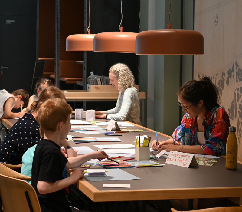 Workshopsituation, bei der zwei Frauen mit Kindern Comics zeichen.