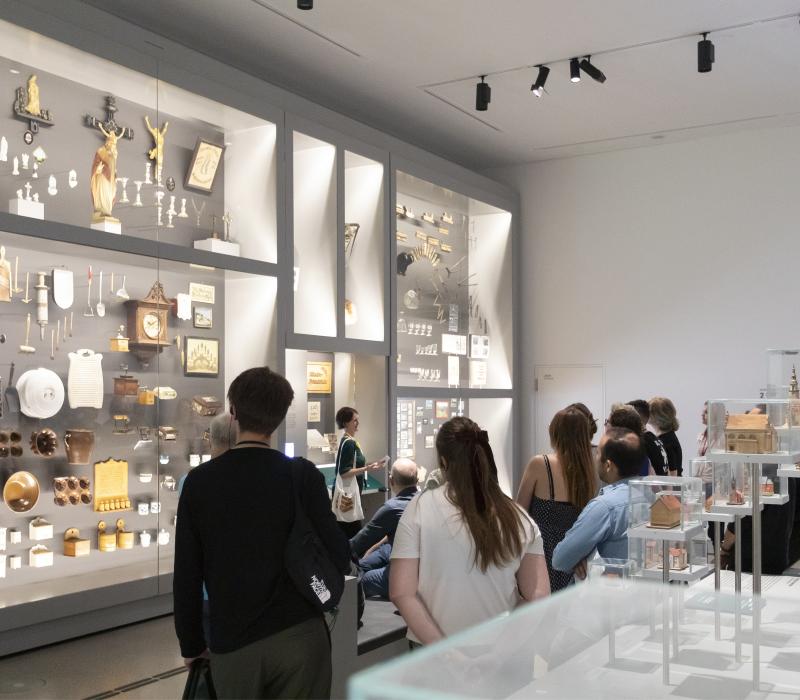 mehrere Personen stehen vor einer Ausstellungswand mit kleinen Objekten